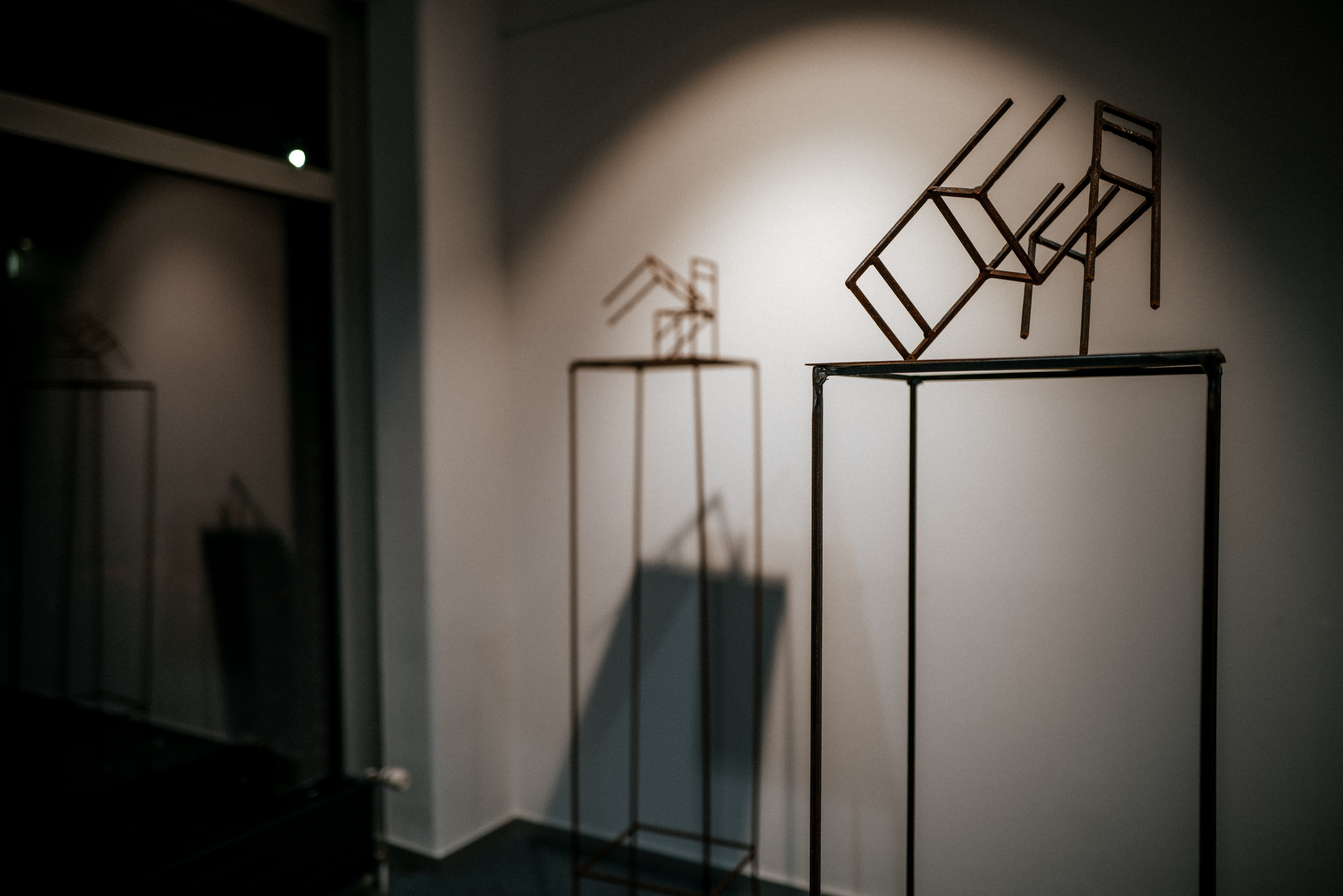 Sculpture of two linear metal chairs with its shadow on the wall