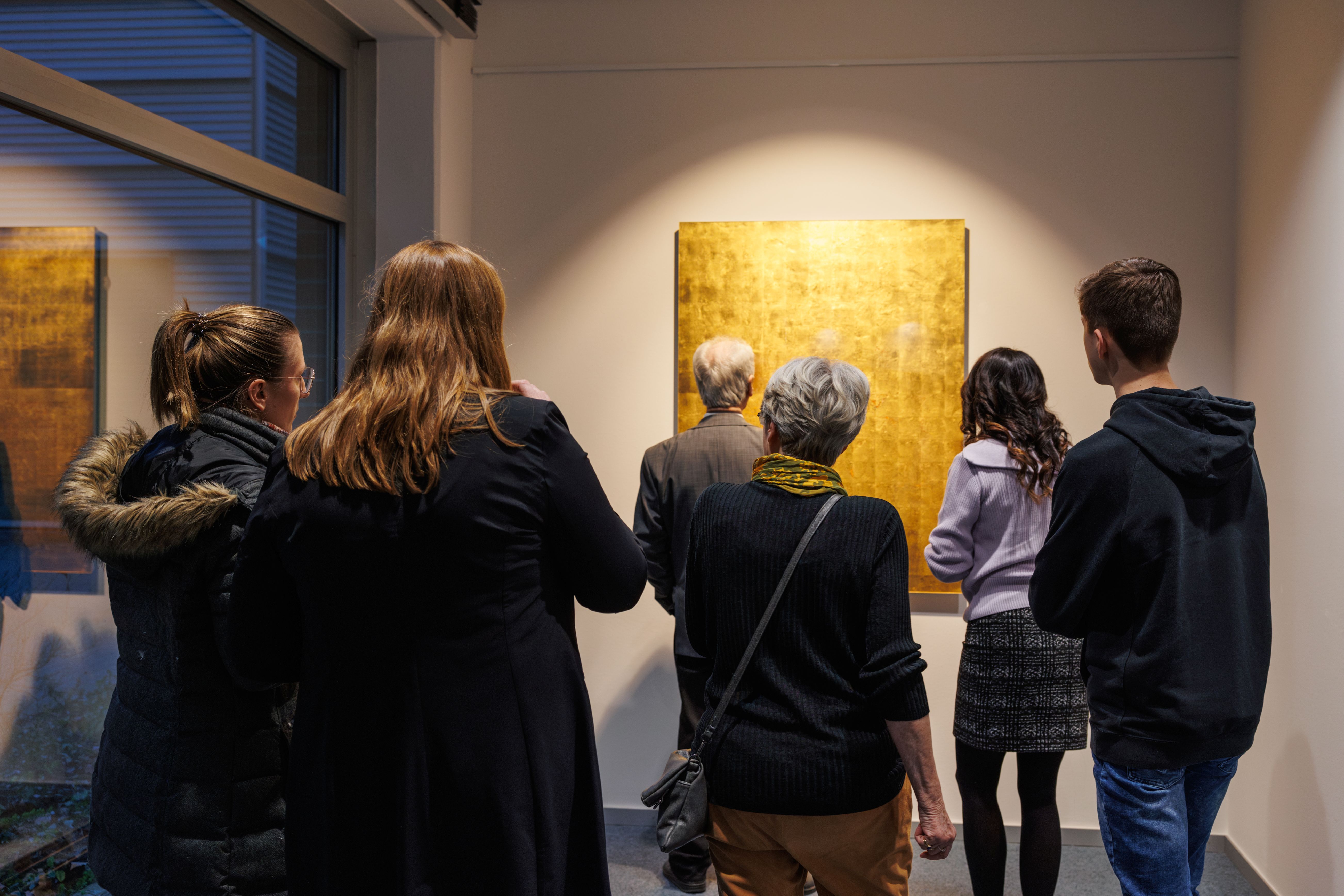People at the finissage of Michael Burges' exhibition in front of a golden artwork