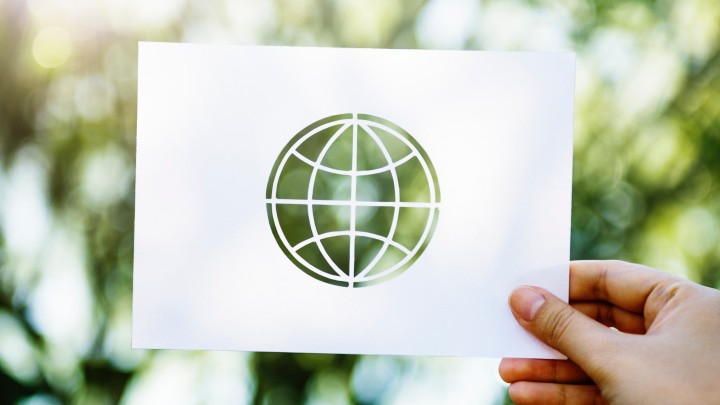 Paper cut of a globe in front of blurry green leaves in the background