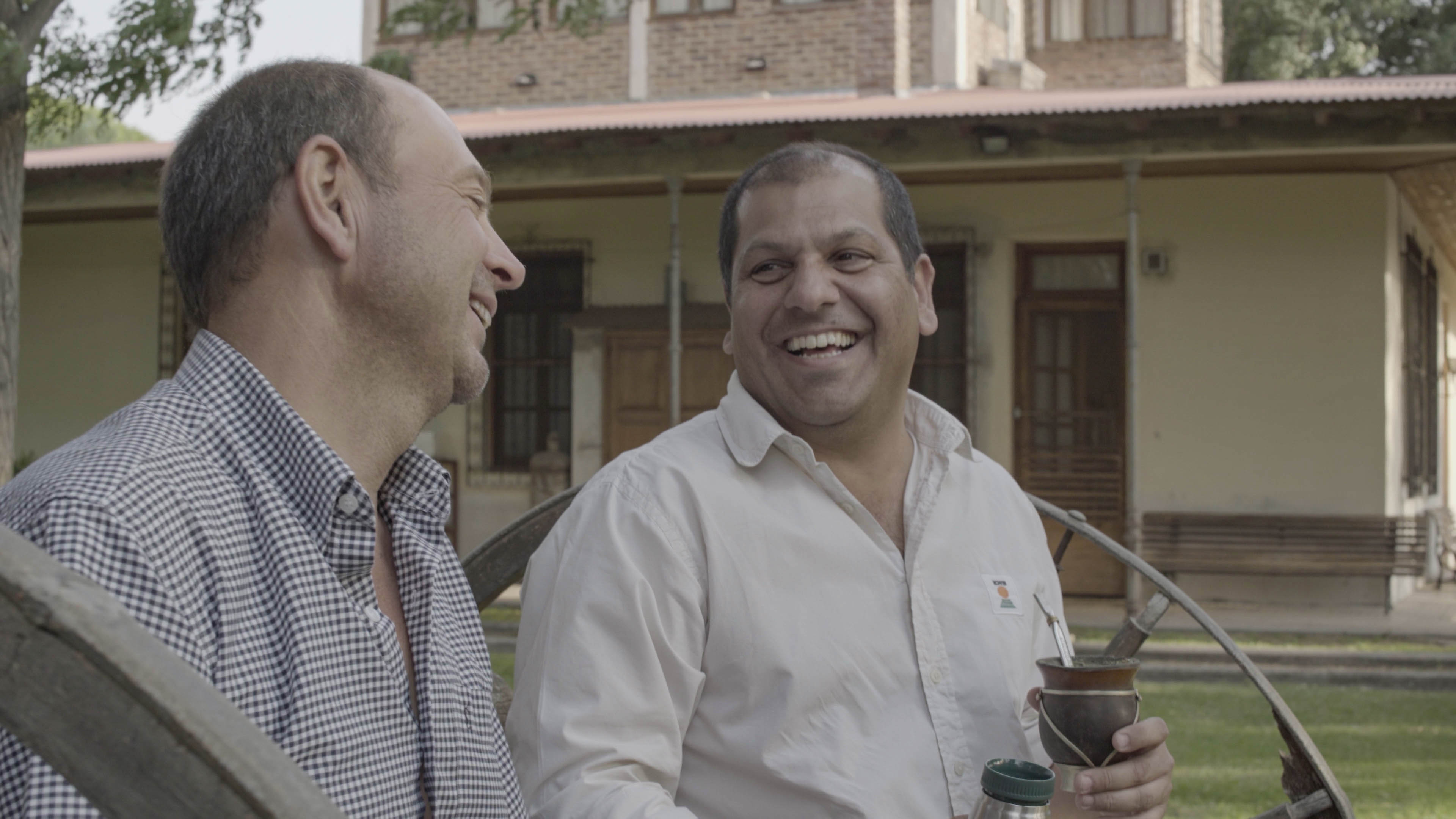 Farmer Luís Parra and KWS consultant Alfonso Caligari sit on a bench together, laughing and enjoying a cup of maté tea.