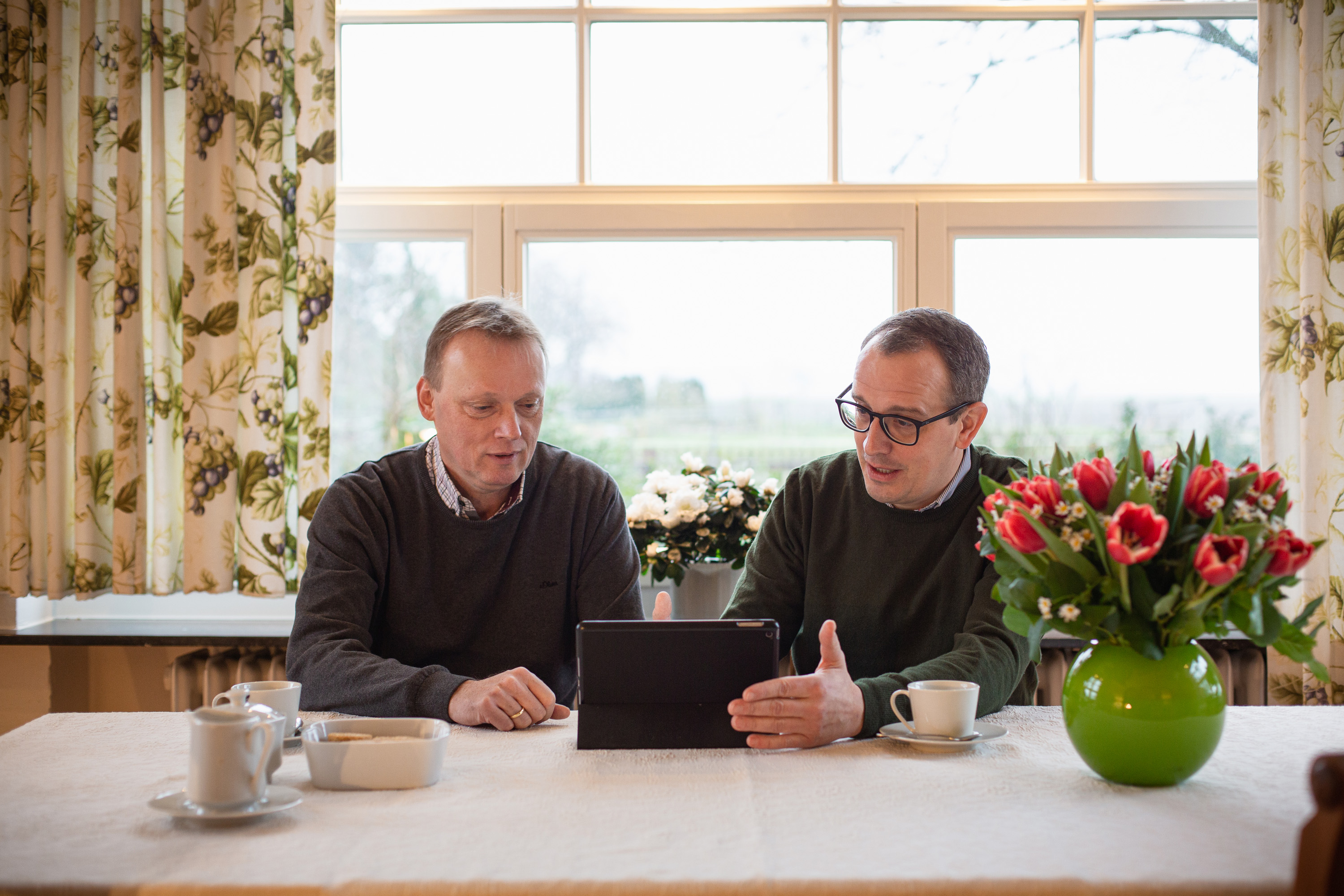 KWS-Saatgutberater Fritz-Jürgen Lutterloh und Landwirt Christian Flögel sitzen am Kaffeetisch und begutachten Daten auf einem iPad.
