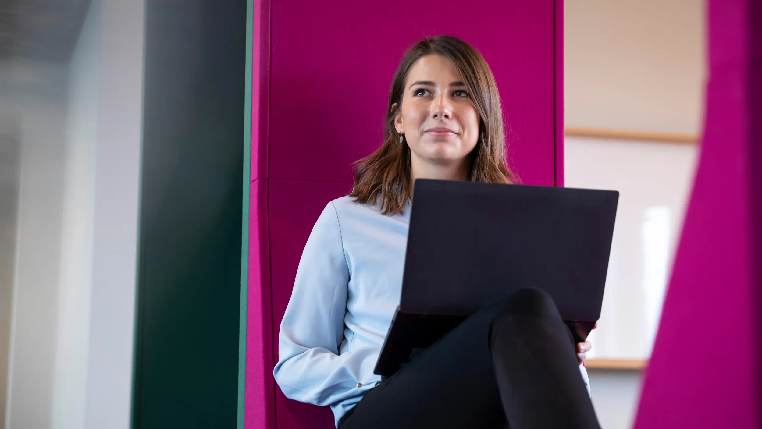 A woman sits in an armchair with a laptop on her lap