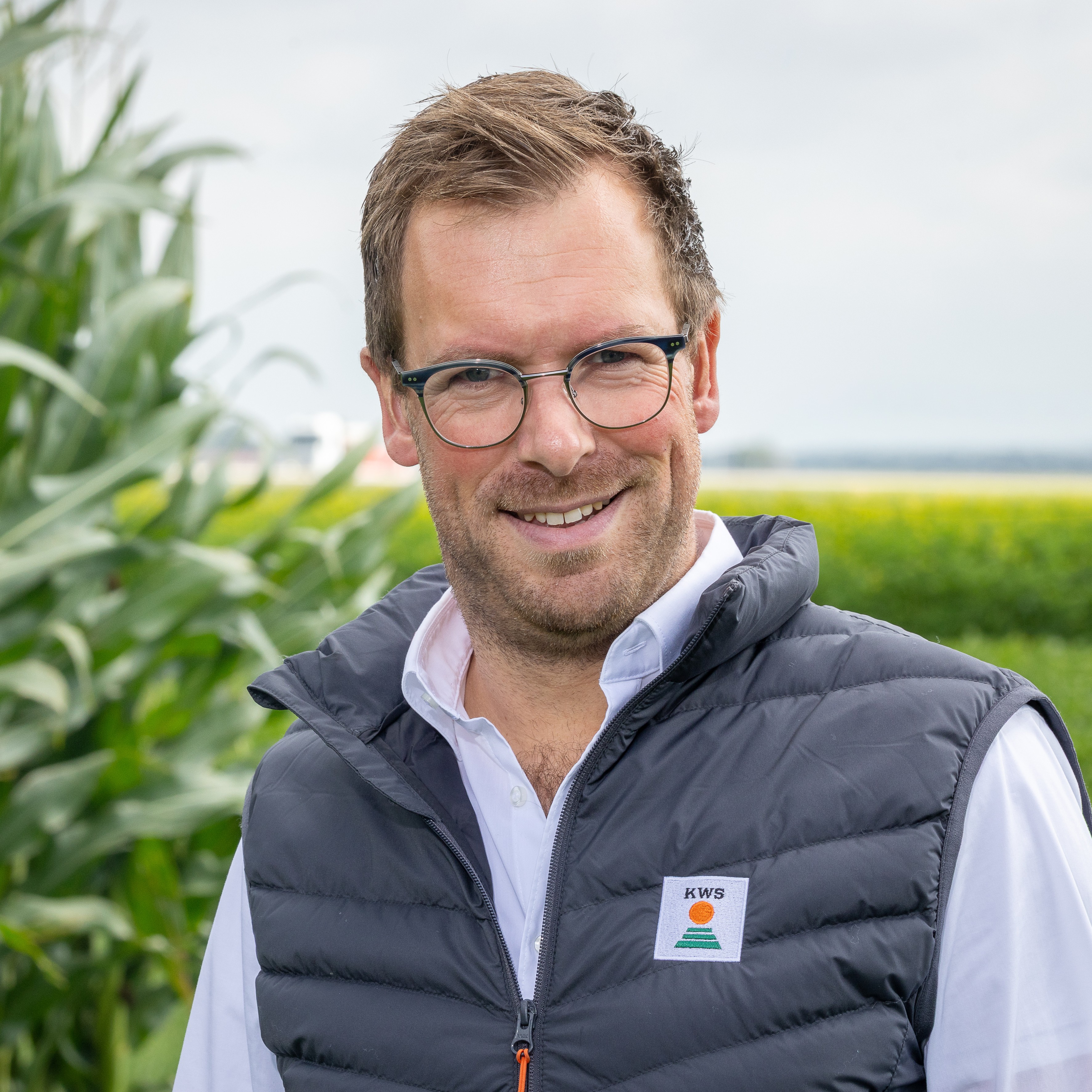Leon Rommens poseert met een glimlach, gekleed in een grijs polo-shirt met een logo. De achtergrond is neutraal en licht.
