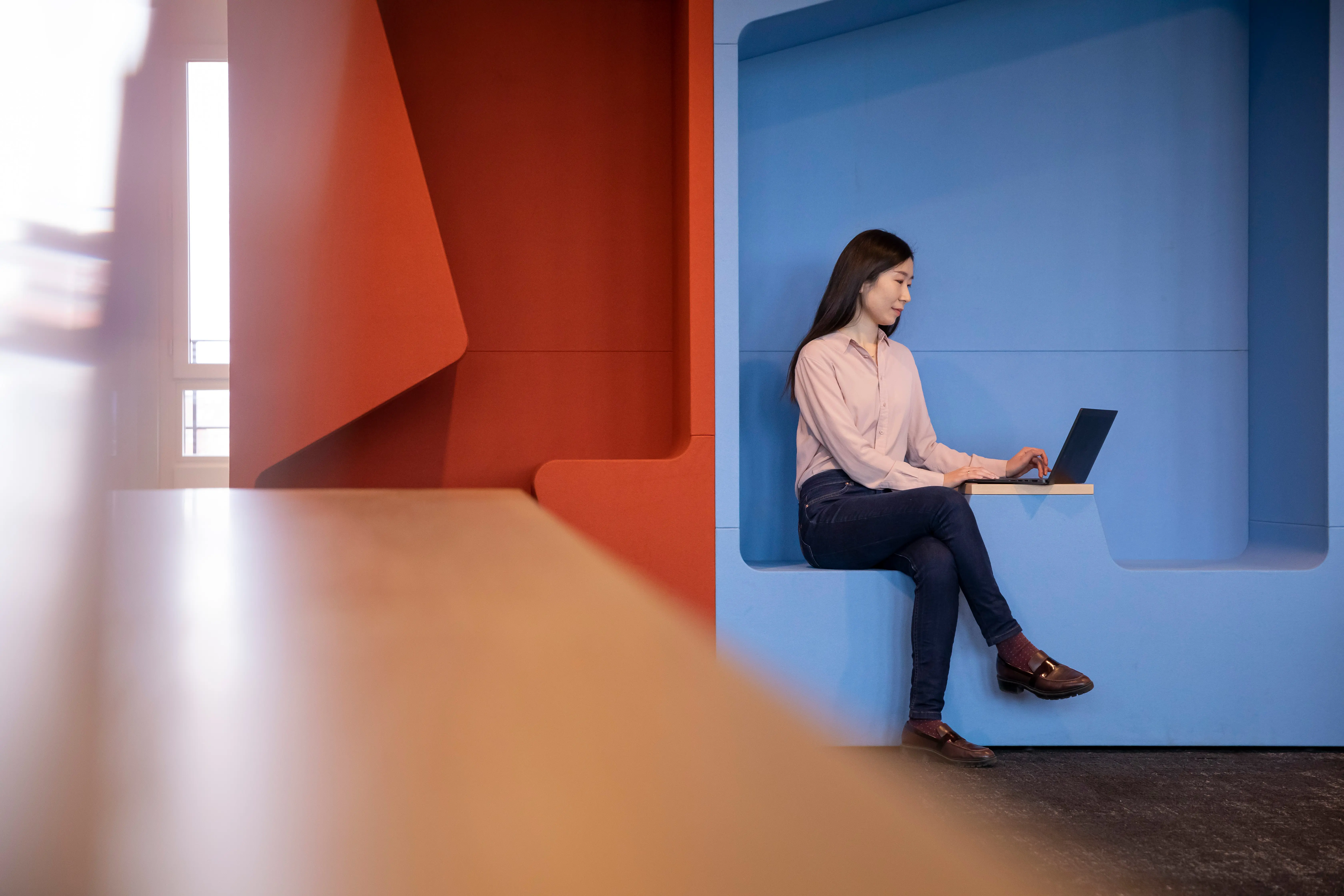 Woman sitting on sofa with laptop in colorful office area