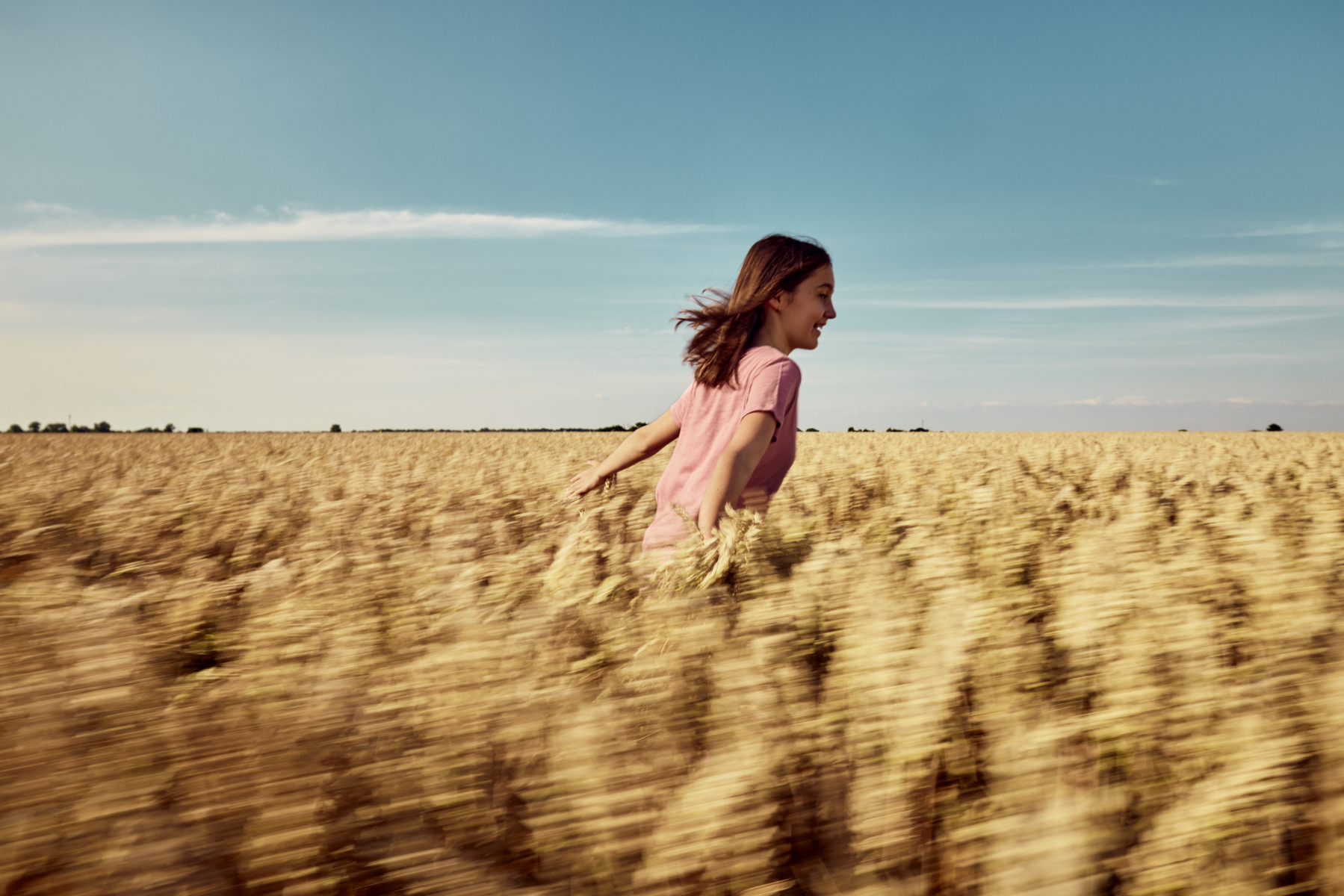 A farmer's daughter runs through a cereal field in summer