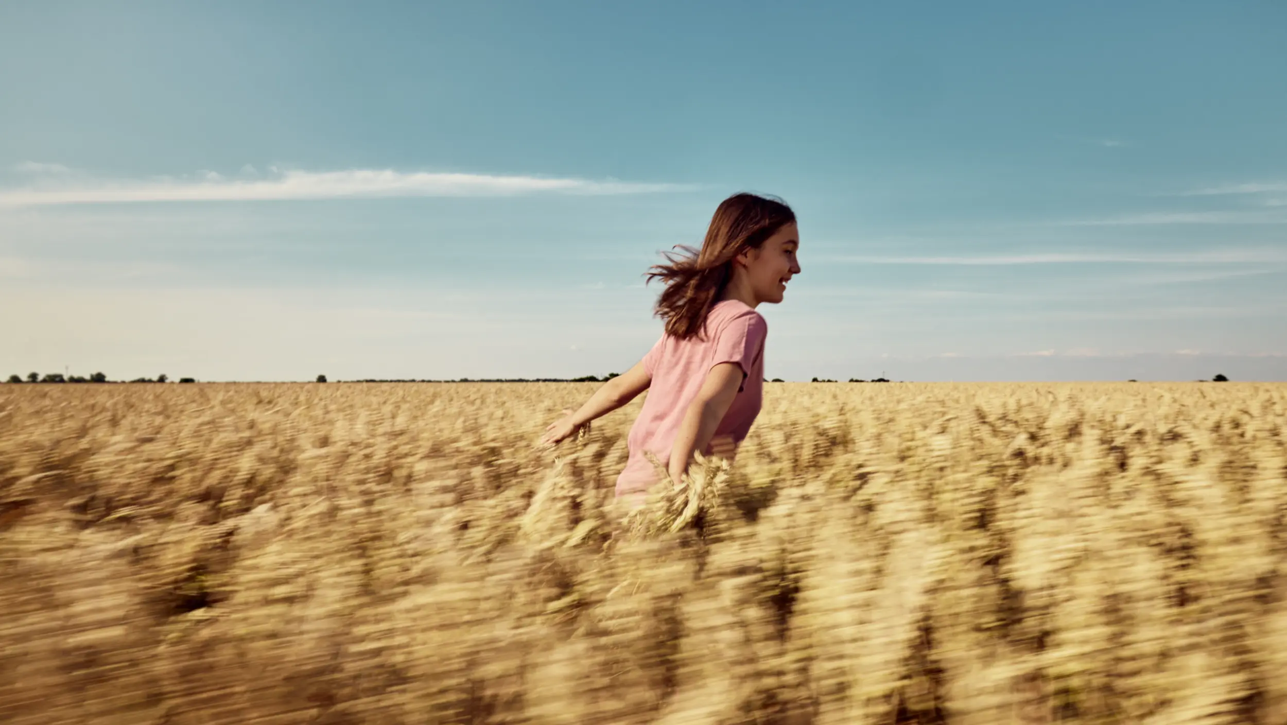 A farmer's daughter runs through a cereal field in summer