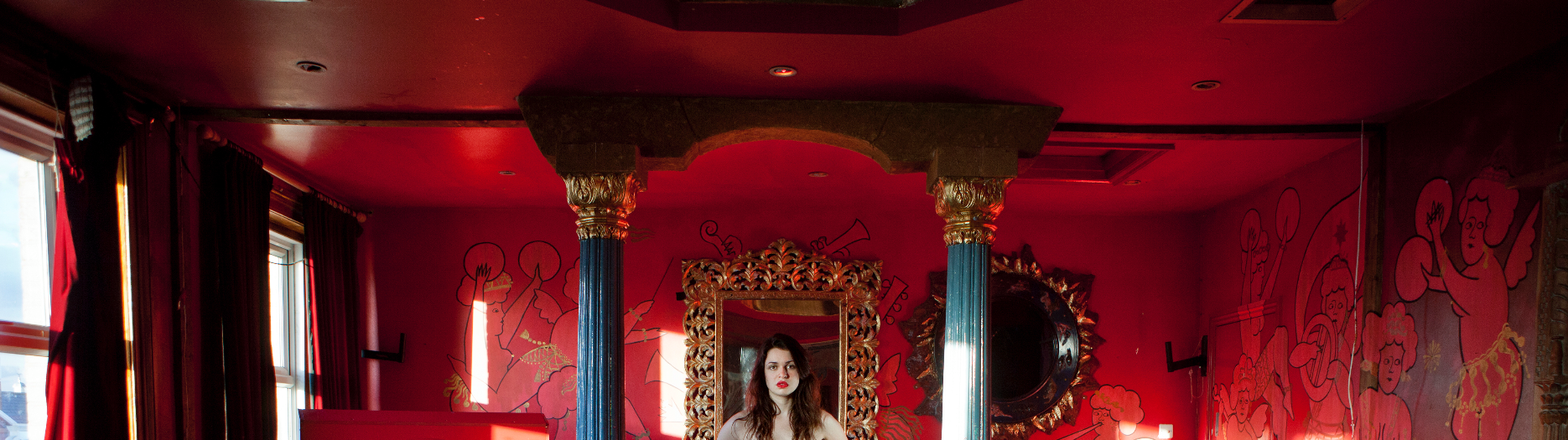 A room in red and gold with a woman looking at you